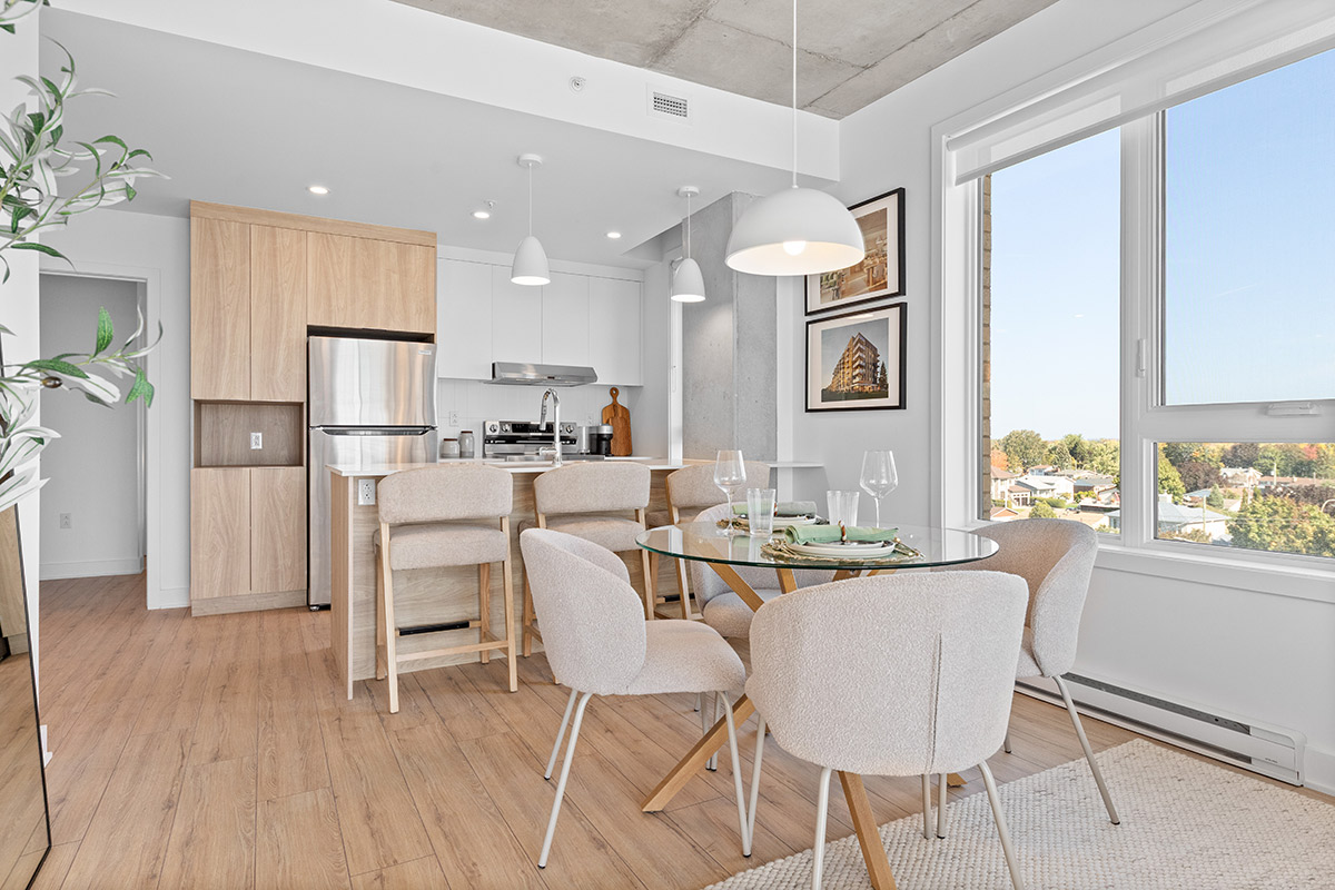 Salle à manger lumineuse et cuisine moderne avec électroménagers en acier inoxydable, armoires en bois pâle et grandes fenêtres offrant une vue dégagée.